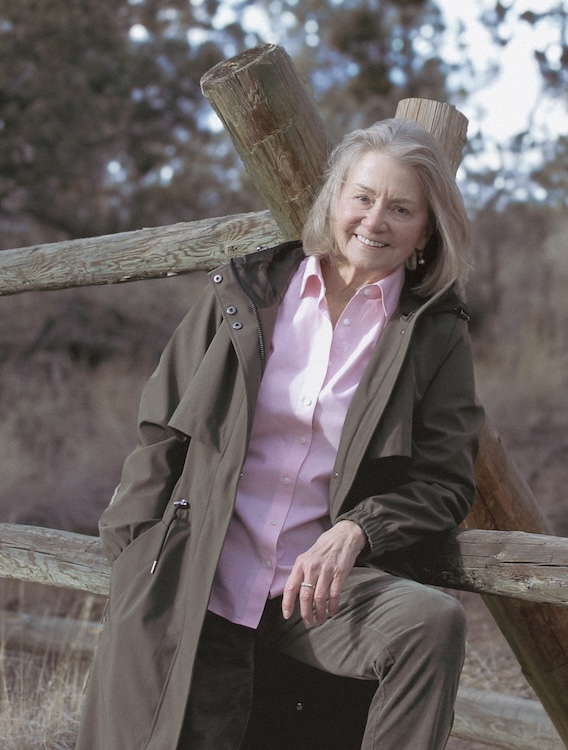 Oregon Poet Laureate Ellen Waterston leans against a wood fence in the desert sun.